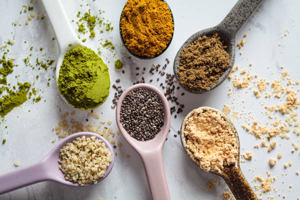 Flat lay of super food powders in spoons, white marble background.